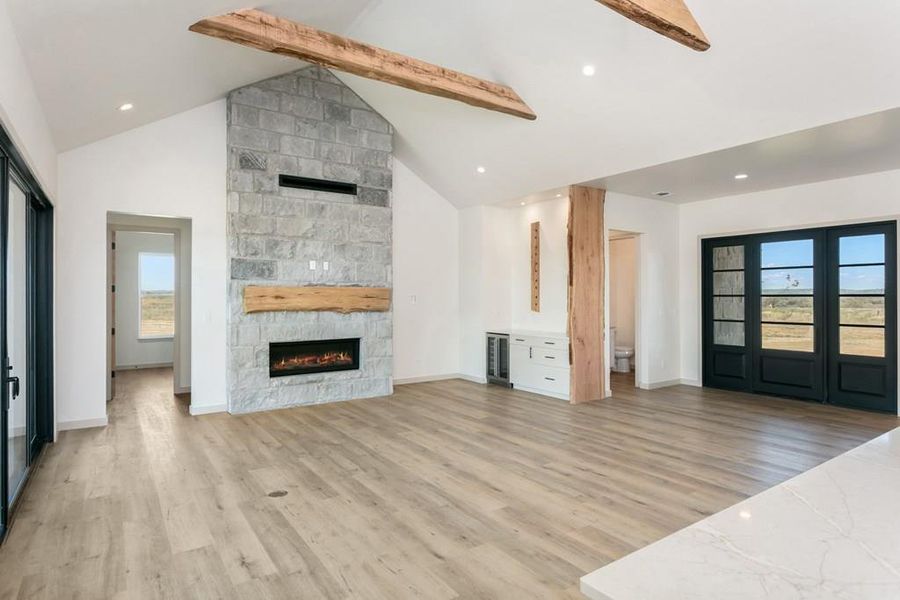 Unfurnished living room with light wood-type flooring, high vaulted ceiling, a stone fireplace, beam ceiling, and recessed lighting Unfurnished living room with light wood-type flooring, high vaulted ceiling, a stone fireplace, beam ceiling, and recessed lighting