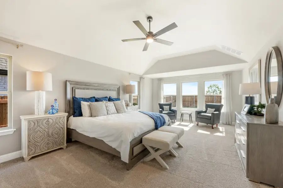 Master bedroom with vaulted ceiling, ceiling fan, carpet flooring, and large windows with seating area