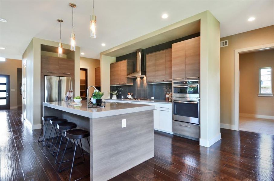 Kitchen featuring wall chimney range hood, modern cabinets, appliances with stainless steel finishes, a breakfast bar, and backsplash Kitchen featuring wall chimney range hood, modern cabinets, appliances with stainless steel finishes, a breakfast bar, and backsplash