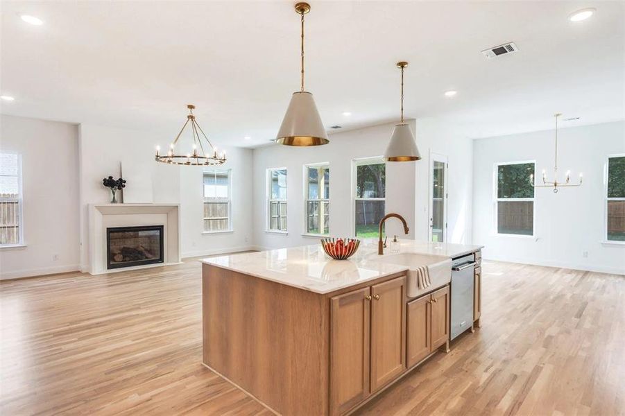 Kitchen with a chandelier, open floor plan, a glass covered fireplace, hanging light fixtures, and an island with sink