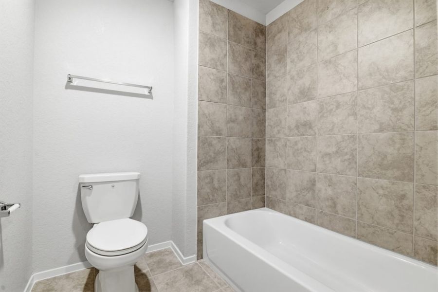 Image of a bathroom with a toilet, and a shower in tub with light brown tile