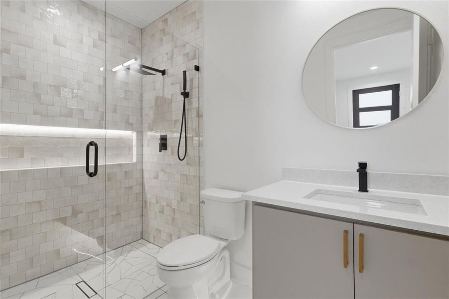 Contemporary bathroom featuring a frameless glass shower enclosure with a built-in illuminated niche, matte black fixtures, and mosaic-style wall tiling Contemporary bathroom featuring a frameless glass shower enclosure with a built-in illuminated niche, matte black fixtures, and mosaic-style wall tiling