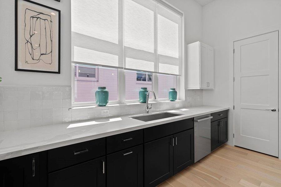 A sleek kitchen features minimalist black cabinetry, white countertops, and light wood flooring. A sleek kitchen features minimalist black cabinetry, white countertops, and light wood flooring.