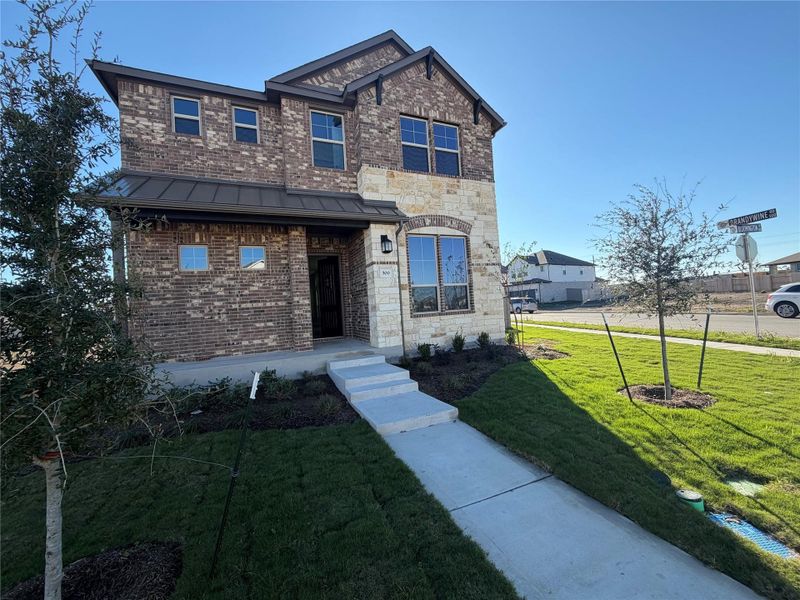 View of front of house featuring a front lawn, brick siding, a standing seam roof, a metal roof, and stone siding View of front of house featuring a front lawn, brick siding, a standing seam roof, a metal roof, and stone siding