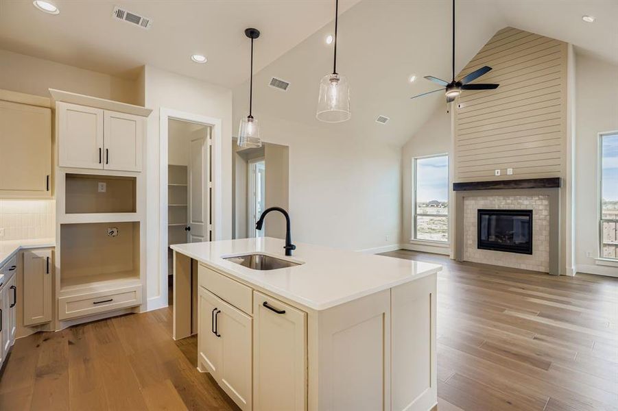 Kitchen featuring a center island with sink, high vaulted ceiling, open floor plan, decorative light fixtures, and light wood-style floors Kitchen featuring a center island with sink, high vaulted ceiling, open floor plan, decorative light fixtures, and light wood-style floors