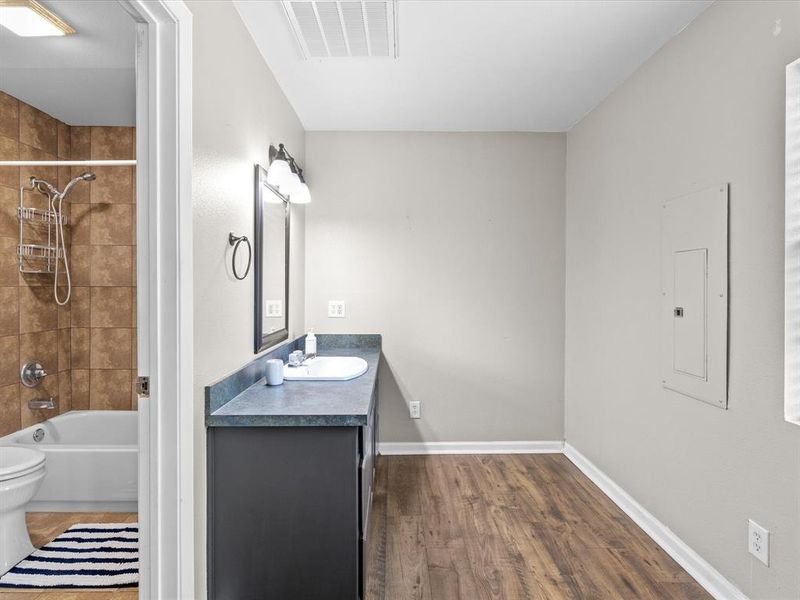 Full bathroom with electric panel, vanity, wood finished floors, and shower / tub combination Full bathroom with electric panel, vanity, wood finished floors, and shower / tub combination