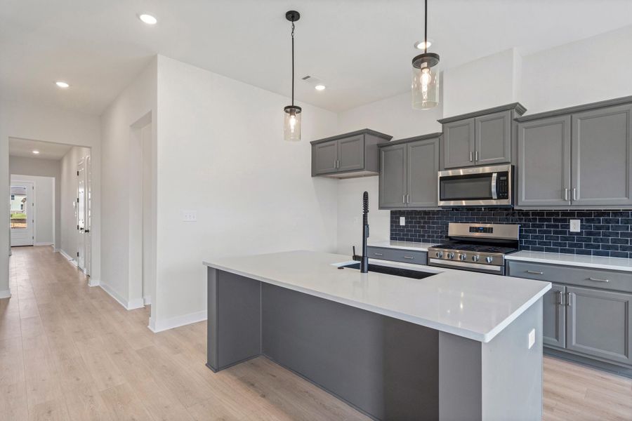Kitchen featuring gray cabinetry, stainless steel appliances, dark subway tile backsplash, and an island with a white countertop