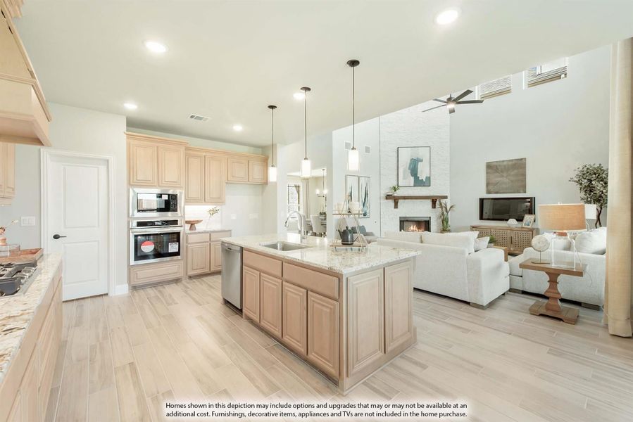 Open-concept kitchen with large island, light wood cabinets, and pendant lights, flowing into a living room with fireplace. Open-concept kitchen with large island, light wood cabinets, and pendant lights, flowing into a living room with fireplace.