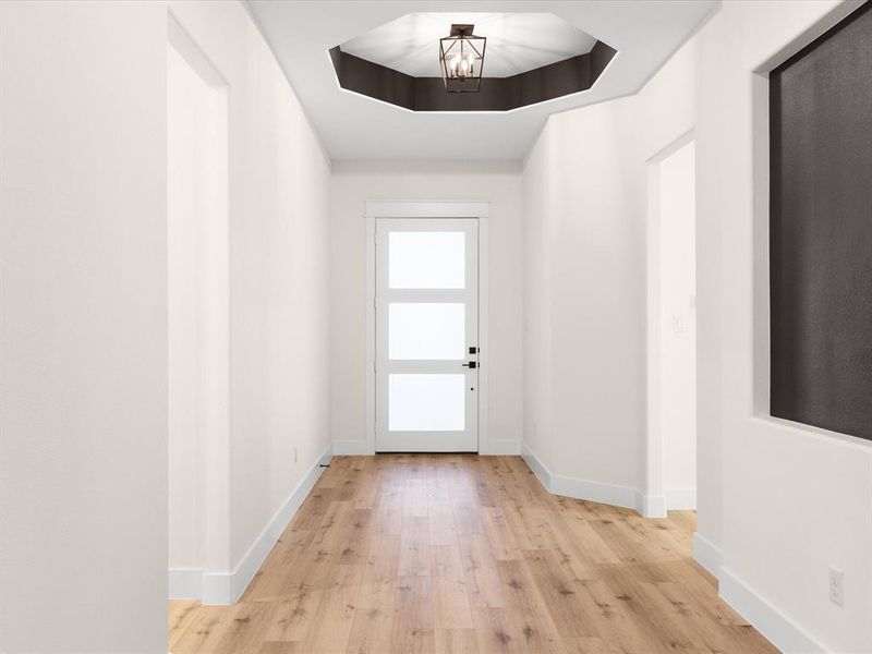 Entryway with wood finished floors, suspended lighting, and a tray ceiling