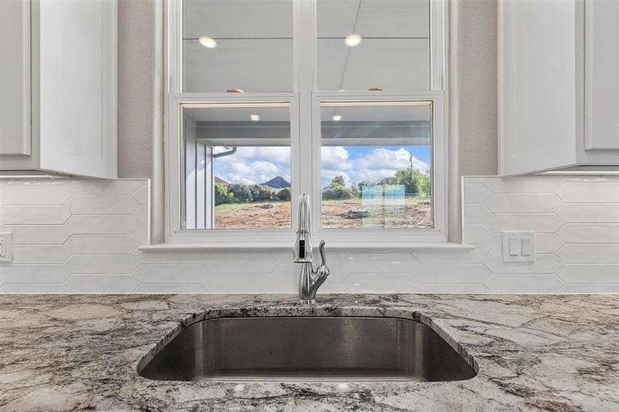 Kitchen with sink, tasteful backsplash, white cabinetry, and light stone counters