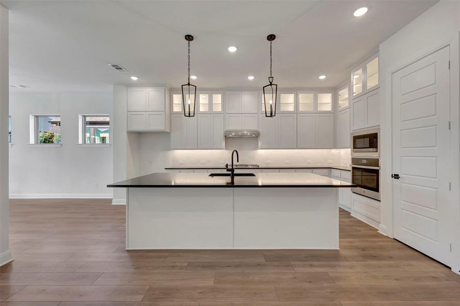 Kitchen featuring white cabinetry, stainless steel appliances, hanging light fixtures, and glass insert cabinets