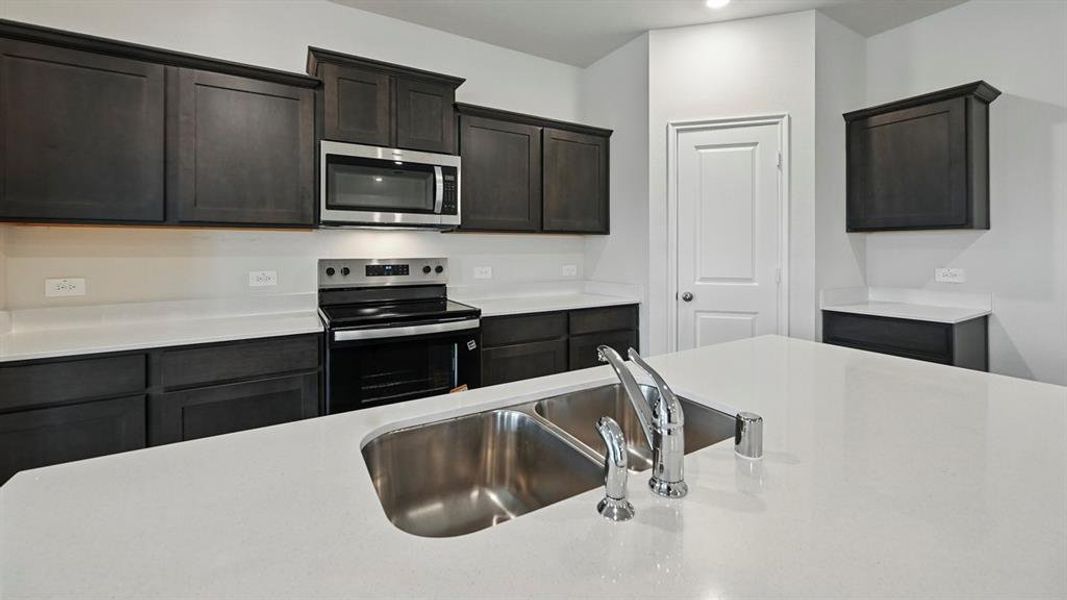 Kitchen featuring an island with a double basin sink, stainless steel faucet, and white countertops