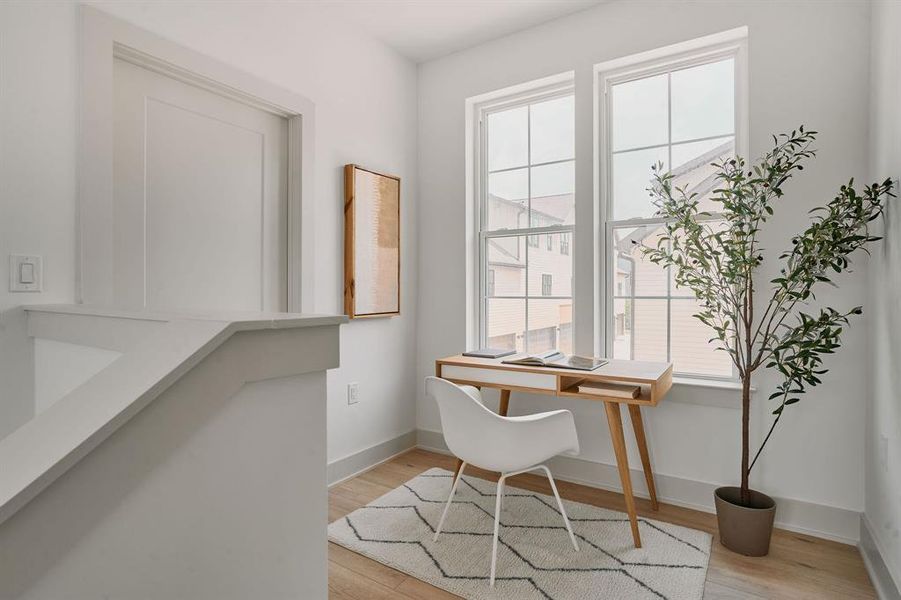 Bright loft space featuring two large windows with grid panes, light wood-finish flooring, and crisp white trim