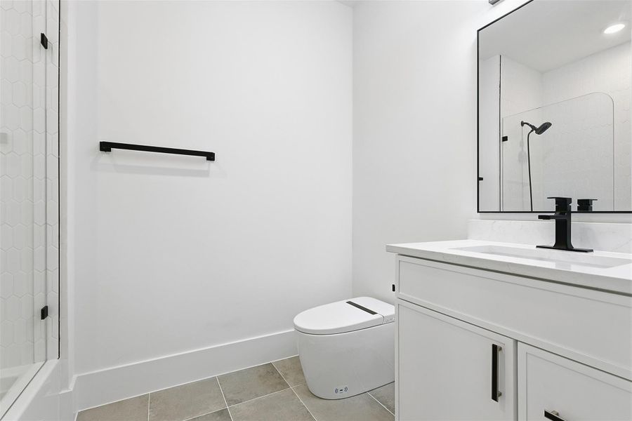 The secondary bathroom offers a clean aesthetic with a white vanity, matte black hardware, and large-format grey floor tiles.