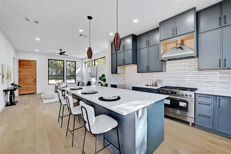 Kitchen with light hardwood / wood-style floors, a kitchen island, pendant lighting, a breakfast bar area, and stainless steel range with gas cooktop