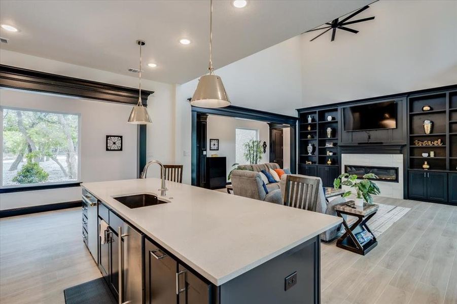 Kitchen featuring light tile floors, hanging light fixtures, a kitchen island with sink, open floor plan, and a glass covered fireplace