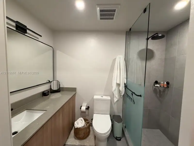 Bathroom featuring a wood-finish vanity with a stone-surface countertop, a frameless glass-enclosed shower with large-format tile surround, and matte black plumbing fixtures