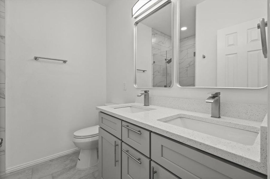 Bathroom featuring double vanity, a stall shower, toilet, and a sink