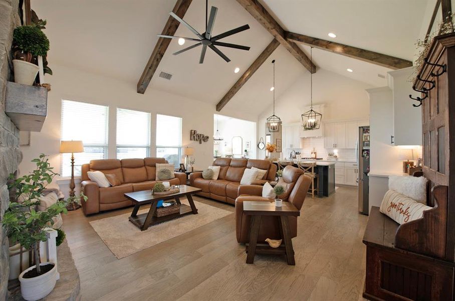 Living room with high vaulted ceiling, ceiling fan, light wood-style floors, beamed ceiling, and a chandelier