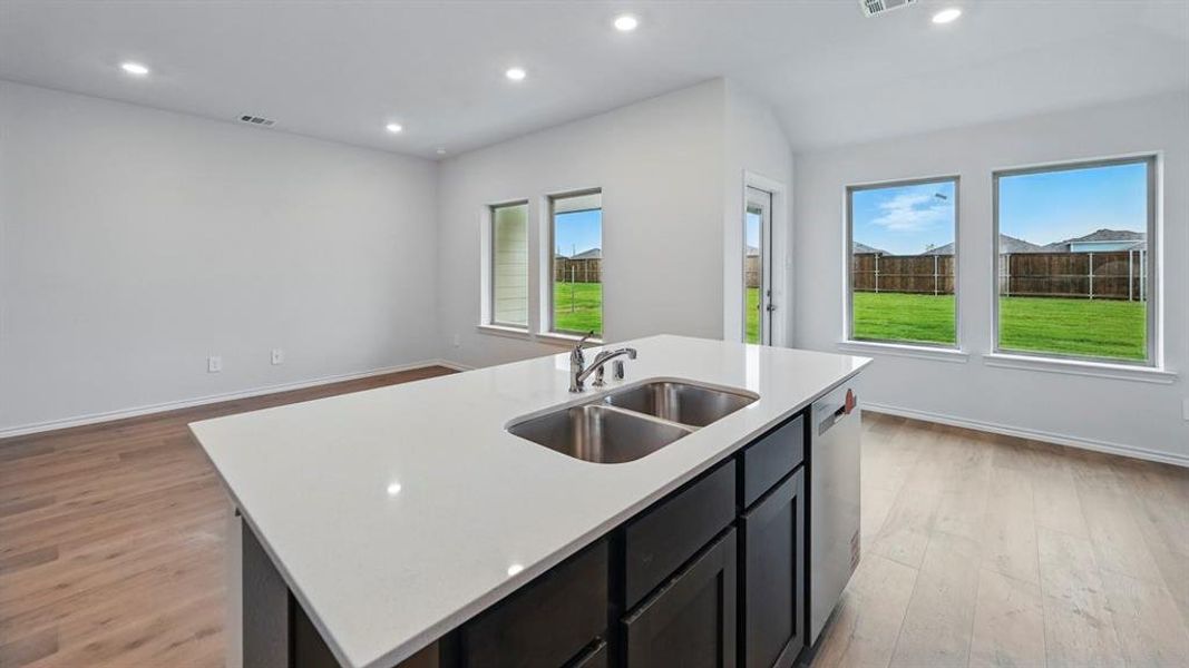 Kitchen featuring dark cabinets, an island with sink, light wood finished floors, recessed lighting, and light stone counters