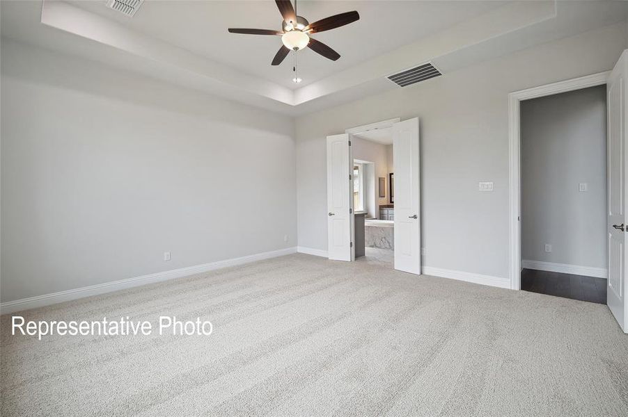 Unfurnished bedroom featuring ceiling fan, light carpet, ensuite bath, and a tray ceiling