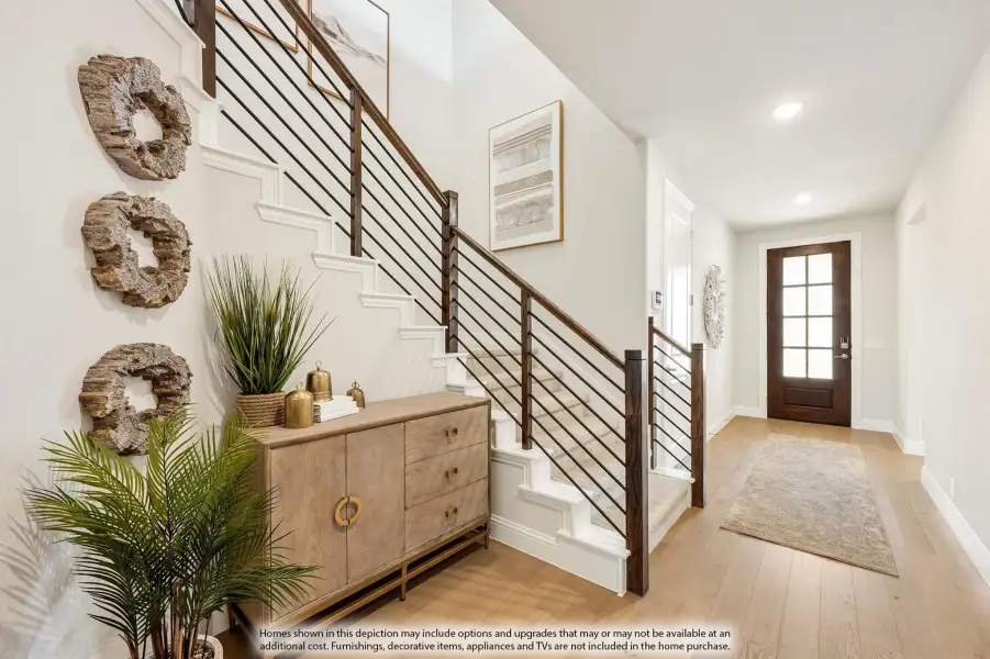 Entryway with staircase, metal railing, wood console table, and front door with light hardwood floors