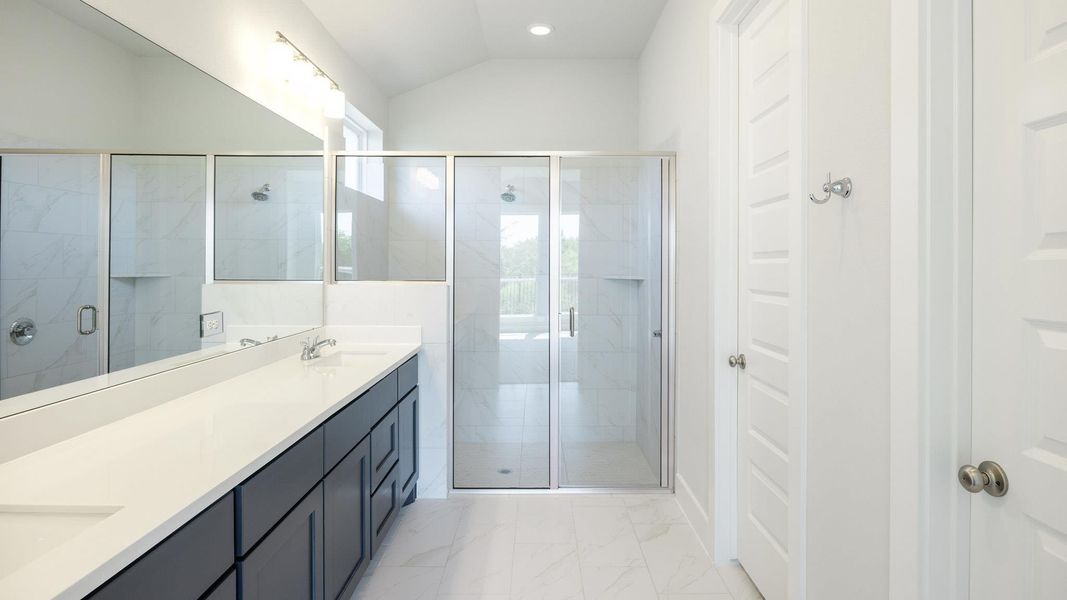 Bathroom featuring double vanity, a shower stall, light marble finish flooring, and lofted ceiling