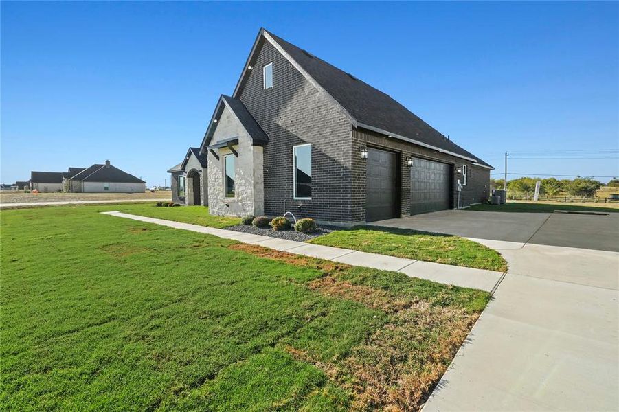 View of side of home with brick siding, a lawn, driveway, and a garage View of side of home with brick siding, a lawn, driveway, and a garage