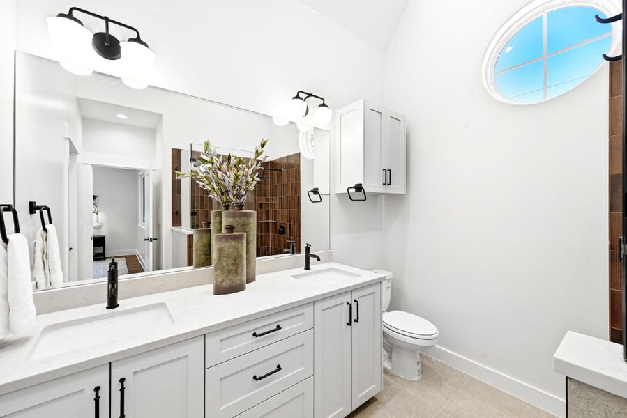 A well-lit primary bathroom features dual vanities, modern fixtures, and a distinctive oval window. A well-lit primary bathroom features dual vanities, modern fixtures, and a distinctive oval window.
