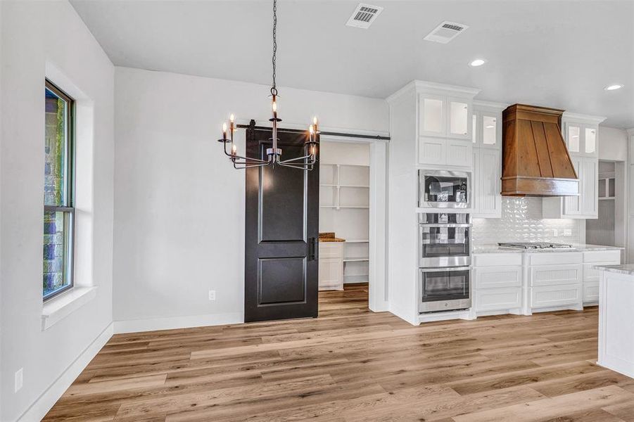 Kitchen with white cabinetry, stainless steel appliances, light hardwood / wood-style flooring, a notable chandelier, and custom exhaust hood