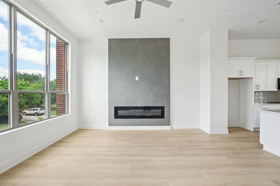 Unfurnished living room featuring healthy amount of natural light, a large fireplace, light wood finished floors, and baseboards
