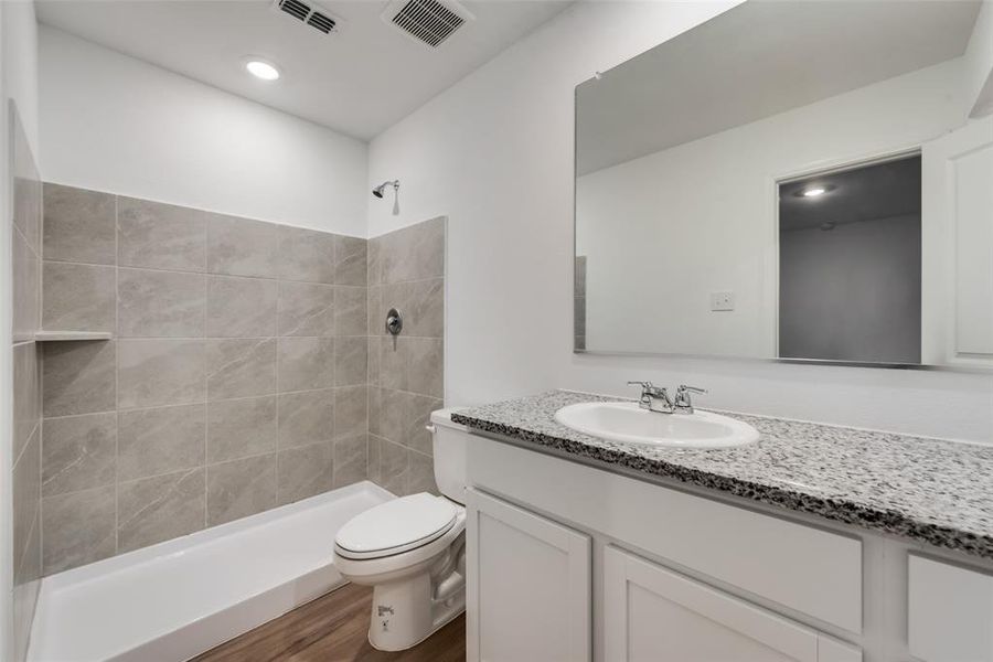 Bathroom featuring a tile shower, vanity, hardwood / wood-style floors, and toilet