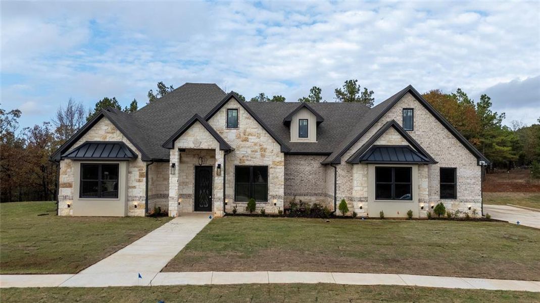 French country style house featuring stone siding, a standing seam roof, and a front lawn