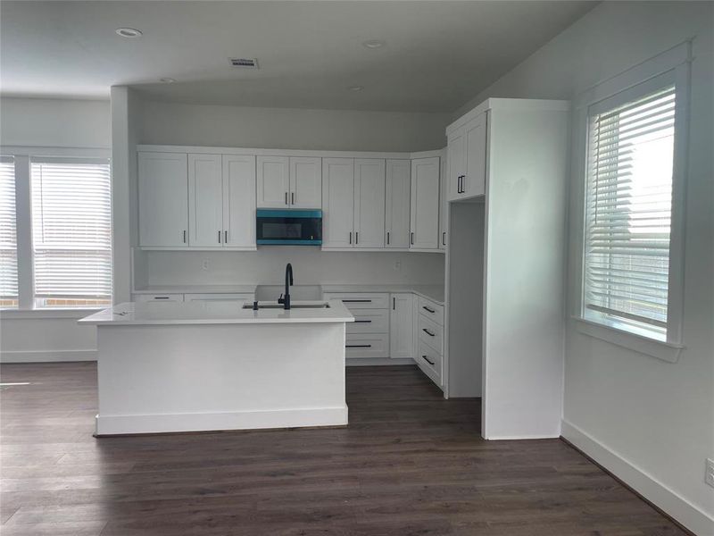 Kitchen featuring healthy amount of natural light, white cabinets, a kitchen island with sink, black microwave, and recessed lighting