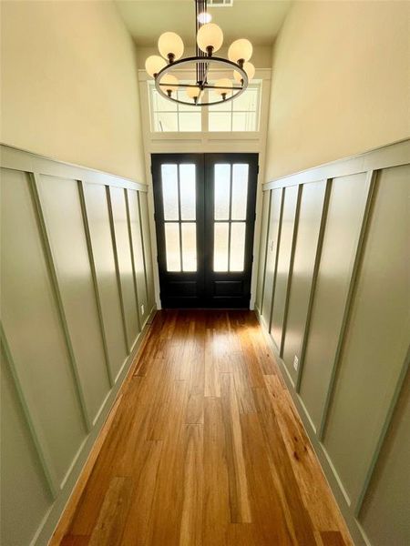Doorway with a decorative wall, wood finished floors, hanging lights, french doors, and a high ceiling