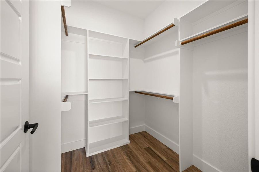 Walk-in closet featuring wood-finish flooring, white built-in shelving, white baseboards, and wood closet rods