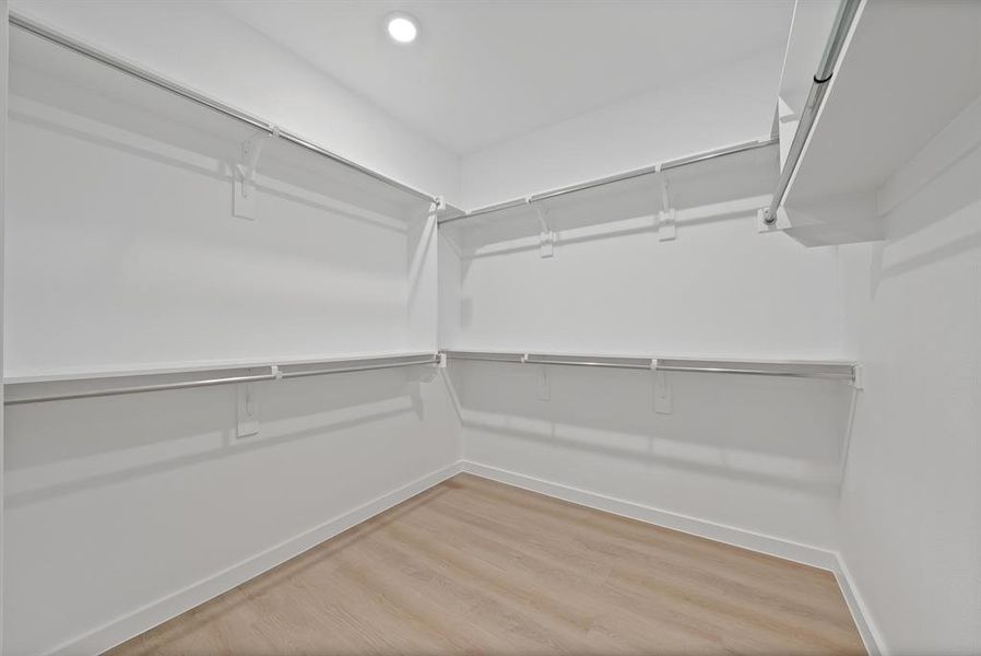 Spacious walk-in closet featuring white walls, light wood-finish flooring, and recessed ceiling lighting Spacious walk-in closet featuring white walls, light wood-finish flooring, and recessed ceiling lighting