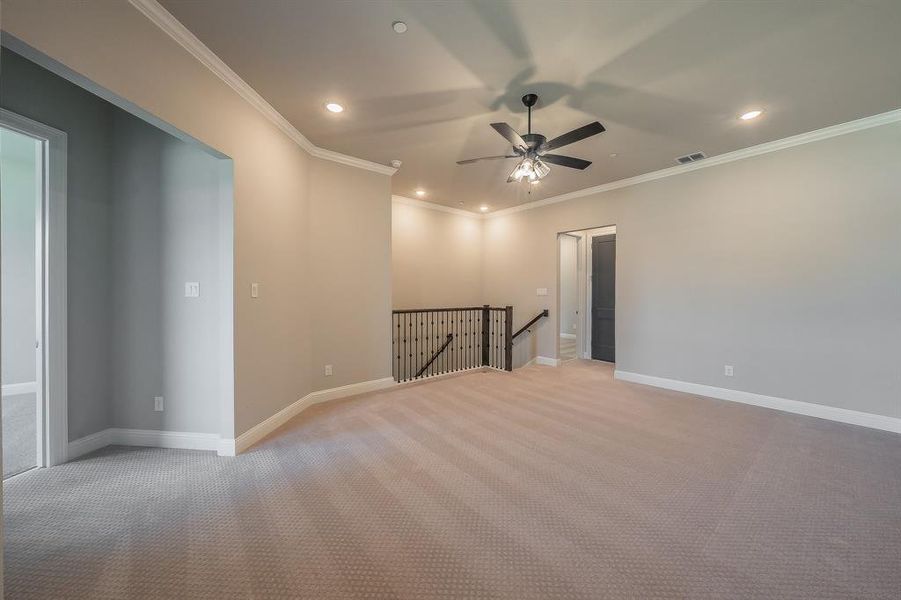 Spacious carpeted landing featuring a ceiling fan, recessed lighting, crown molding, and an iron baluster railing