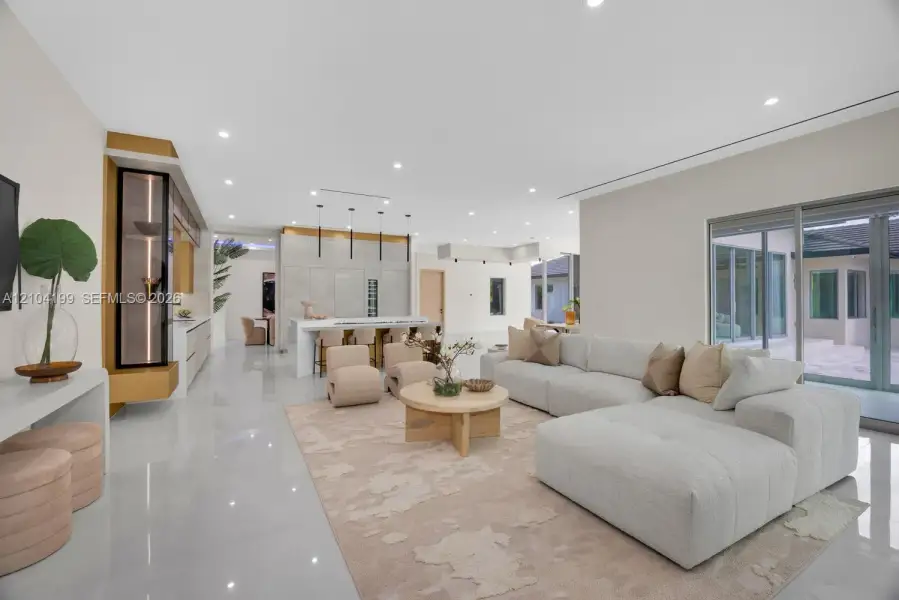 Open-concept interior featuring large-format tile flooring, recessed ceiling lighting, a waterfall-edge kitchen island, metallic accent detailing, and multi-panel sliding glass doors