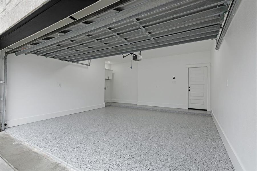 This is a clean and spacious two-car garage featuring a freshly painted interior and an epoxy-coated floor. It includes an automatic door opener and has a side door for convenient access.