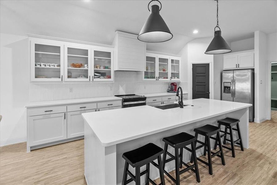 Kitchen with decorative backsplash, appliances with stainless steel finishes, light wood-type flooring, and a sink