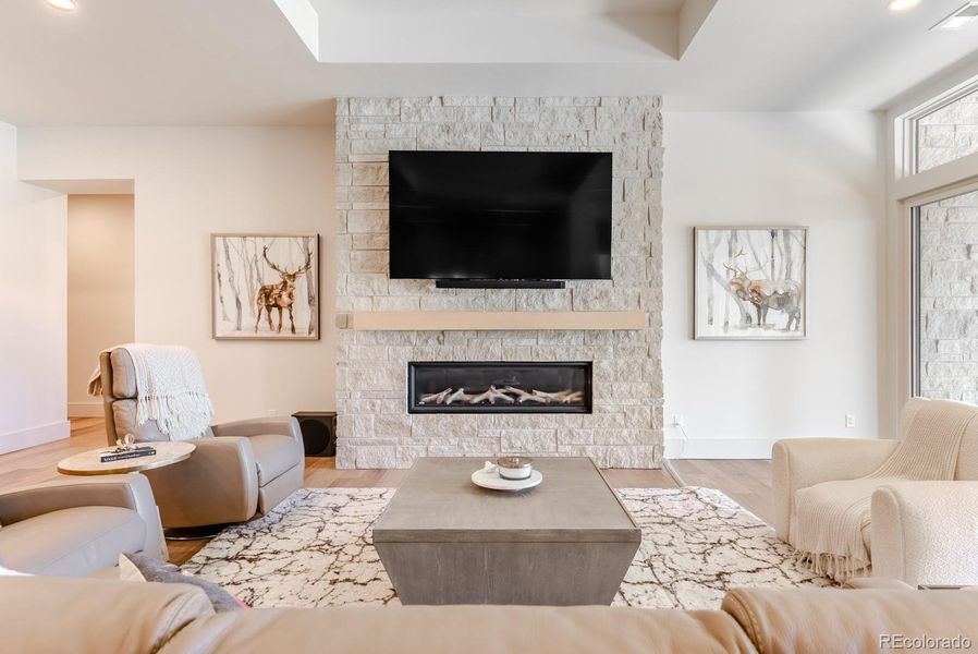 The media lounge is anchored by a stunning floor-to-ceiling linear fireplace wrapped in flagstone, mirroring the home’s exterior materials and reinforcing the intentional architectural connection between indoors and out.