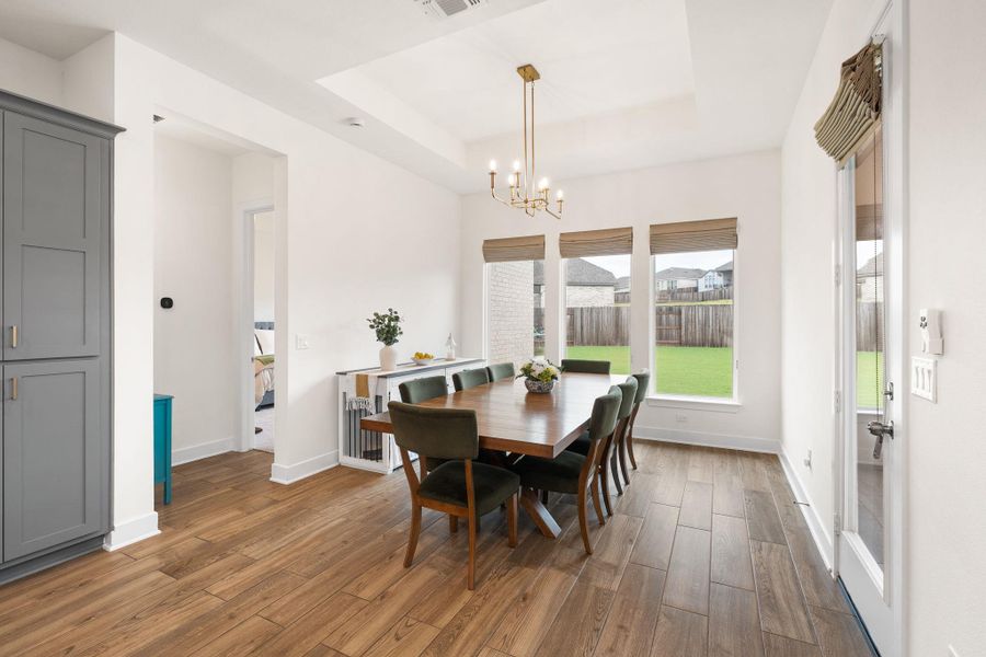 A refined dining space features a sophisticated tray ceiling and warm hardwood flooring.