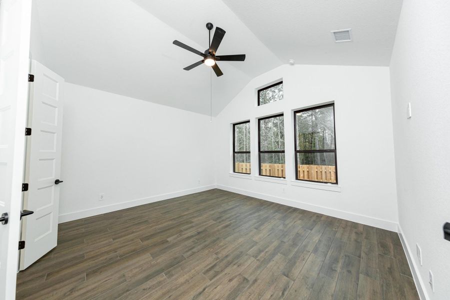 Relax and unwind after a long day in this impressive primary suite! This generously sized room offers the same wood look tile flooring, neutral-toned paint, cathedral ceilings with a ceiling fan, and large windows for added comfort and tranquility.