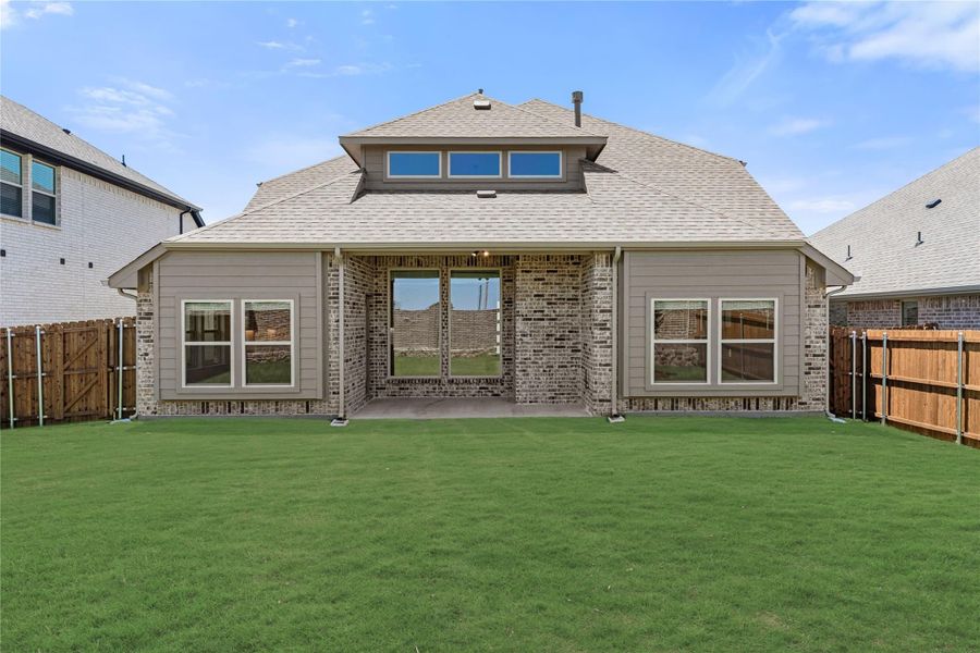 Rear exterior of single-story home with brick and siding, covered patio, and fenced backyard with green lawn.