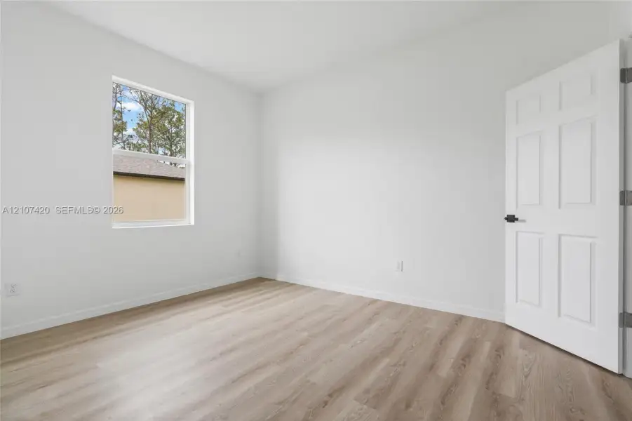 Neutral interior featuring wood-finish flooring, a single-hung window, and a six-panel door with matte black hardware Neutral interior featuring wood-finish flooring, a single-hung window, and a six-panel door with matte black hardware