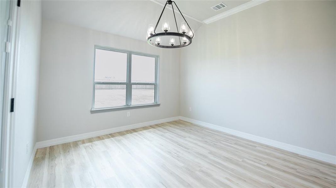 Unfurnished room featuring light wood finished floors, a chandelier, and crown molding Unfurnished room featuring light wood finished floors, a chandelier, and crown molding