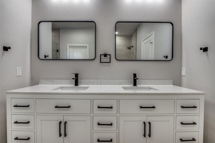 Bathroom featuring a textured wall, double vanity, and a tile shower Bathroom featuring a textured wall, double vanity, and a tile shower