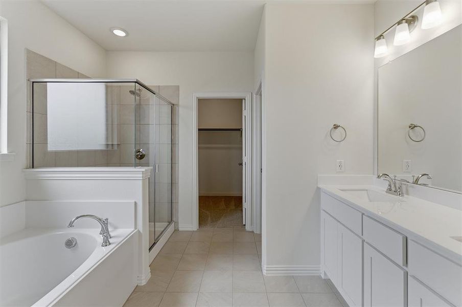 Bathroom featuring a dual vanity with white cabinetry and integrated sinks, a separate walk-in shower with glass enclosure, a built-in soaking tub, and tile flooring