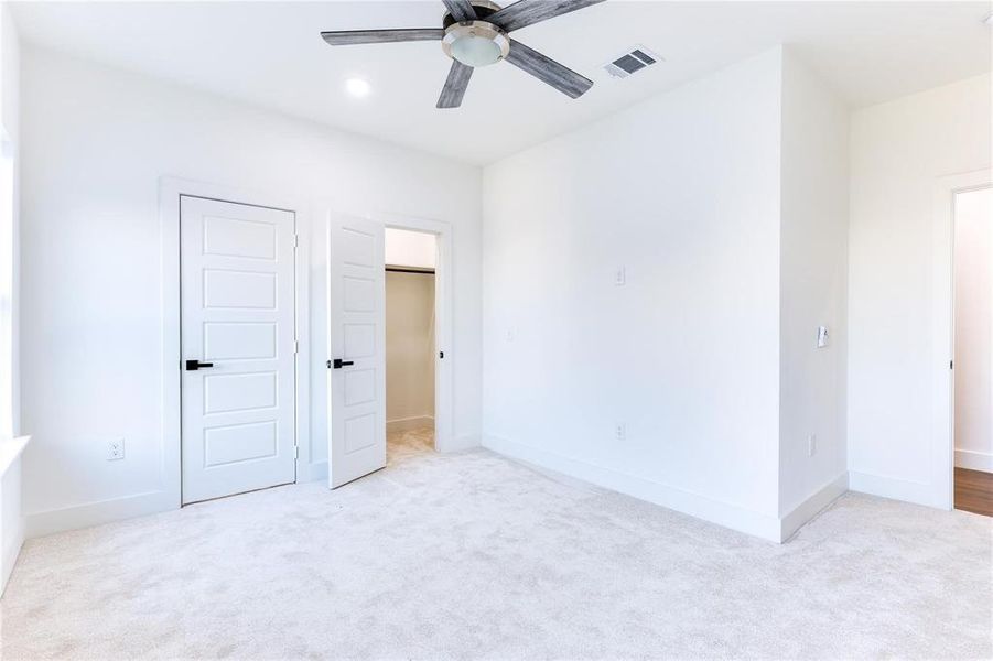 Unfurnished bedroom featuring a spacious closet, light colored carpet, a closet, and ceiling fan